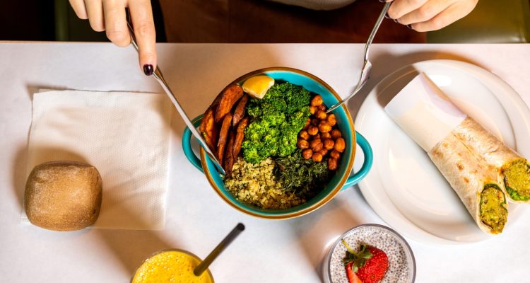 person holding silver spoon and blue ceramic bowl with food